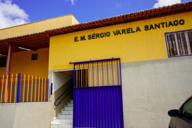 A imagem mostra uma criança sorridente, usando óculos e uma camisa branca com detalhes em azul, ...