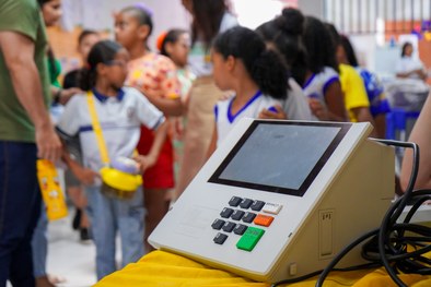 A imagem mostra uma criança sorridente, usando óculos e uma camisa branca com detalhes em azul, ...