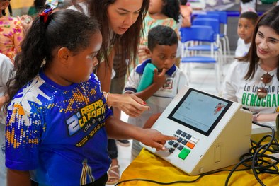 A imagem mostra uma criança sorridente, usando óculos e uma camisa branca com detalhes em azul, ...