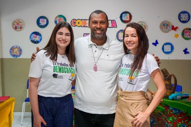 A imagem mostra uma criança sorridente, usando óculos e uma camisa branca com detalhes em azul, ...