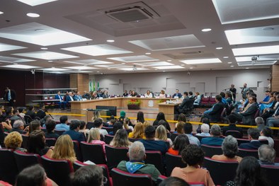 A imagem mostra o palco do plenário do TRE-RN e parte da plateia, com todos de pé, em posição de...