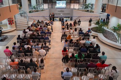 A imagem mostra o palco do plenário do TRE-RN e parte da plateia, com todos de pé, em posição de...