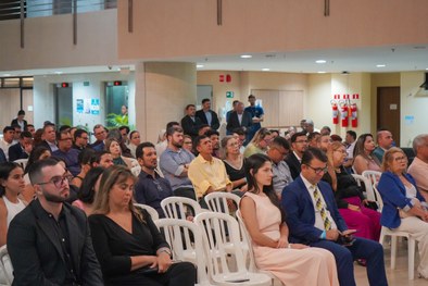 A imagem mostra o palco do plenário do TRE-RN e parte da plateia, com todos de pé, em posição de...