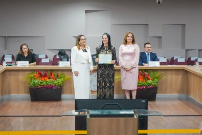 A imagem mostra o palco do plenário do TRE-RN e parte da plateia, com todos de pé, em posição de...