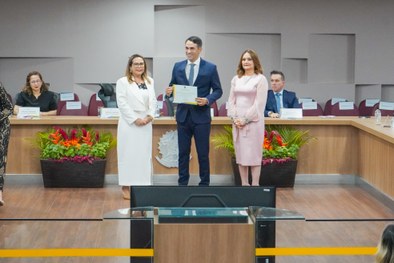 A imagem mostra o palco do plenário do TRE-RN e parte da plateia, com todos de pé, em posição de...