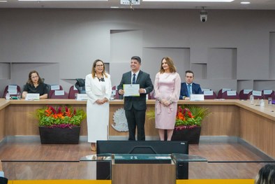 A imagem mostra o palco do plenário do TRE-RN e parte da plateia, com todos de pé, em posição de...