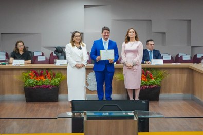 A imagem mostra o palco do plenário do TRE-RN e parte da plateia, com todos de pé, em posição de...