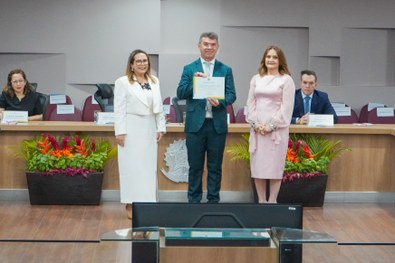 A imagem mostra o palco do plenário do TRE-RN e parte da plateia, com todos de pé, em posição de...