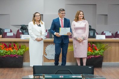 A imagem mostra o palco do plenário do TRE-RN e parte da plateia, com todos de pé, em posição de...