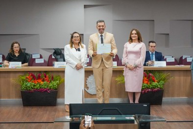 A imagem mostra o palco do plenário do TRE-RN e parte da plateia, com todos de pé, em posição de...