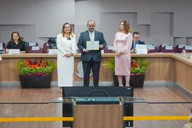 A imagem mostra o palco do plenário do TRE-RN e parte da plateia, com todos de pé, em posição de...