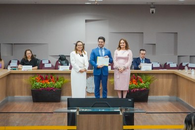 A imagem mostra o palco do plenário do TRE-RN e parte da plateia, com todos de pé, em posição de...