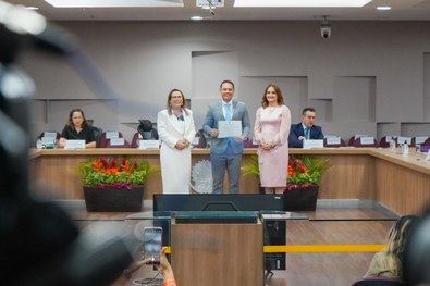 A imagem mostra o palco do plenário do TRE-RN e parte da plateia, com todos de pé, em posição de...