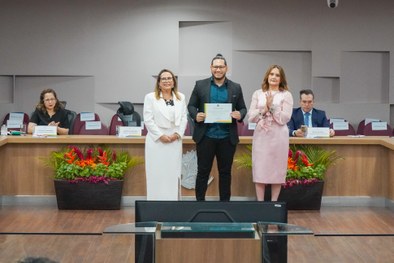 A imagem mostra o palco do plenário do TRE-RN e parte da plateia, com todos de pé, em posição de...