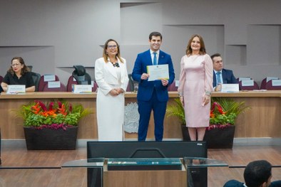 A imagem mostra o palco do plenário do TRE-RN e parte da plateia, com todos de pé, em posição de...