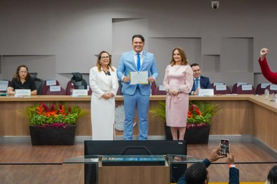 A imagem mostra o palco do plenário do TRE-RN e parte da plateia, com todos de pé, em posição de...