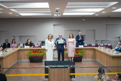 A imagem mostra o palco do plenário do TRE-RN e parte da plateia, com todos de pé, em posição de...